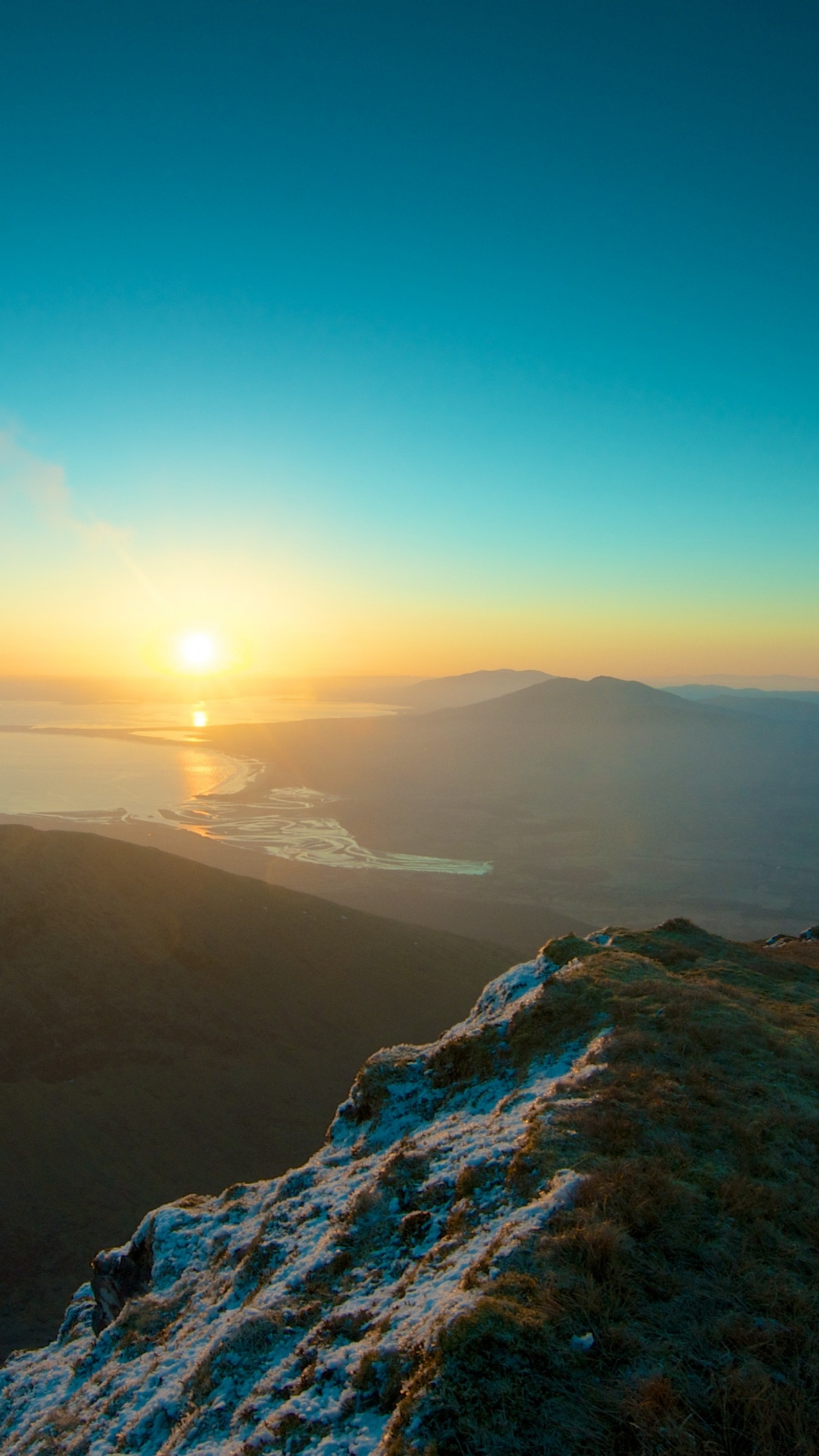 Arafed view of a person standing on a mountain top with a view of the ocean (lake, mountain, sun, sunset, view)