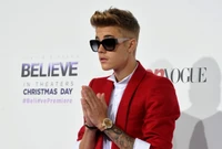 Justin Bieber em um terno vermelho e óculos de sol oversized, fazendo uma pose estilosa em um evento de estreia.