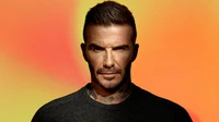 David Beckham avec une expression concentrée, affichant une barbe bien entretenue et une coiffure élégante sur un fond vibrant et coloré.