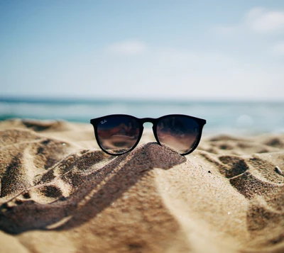 Lunettes de soleil élégantes reposant sur le sable ensoleillé à la plage