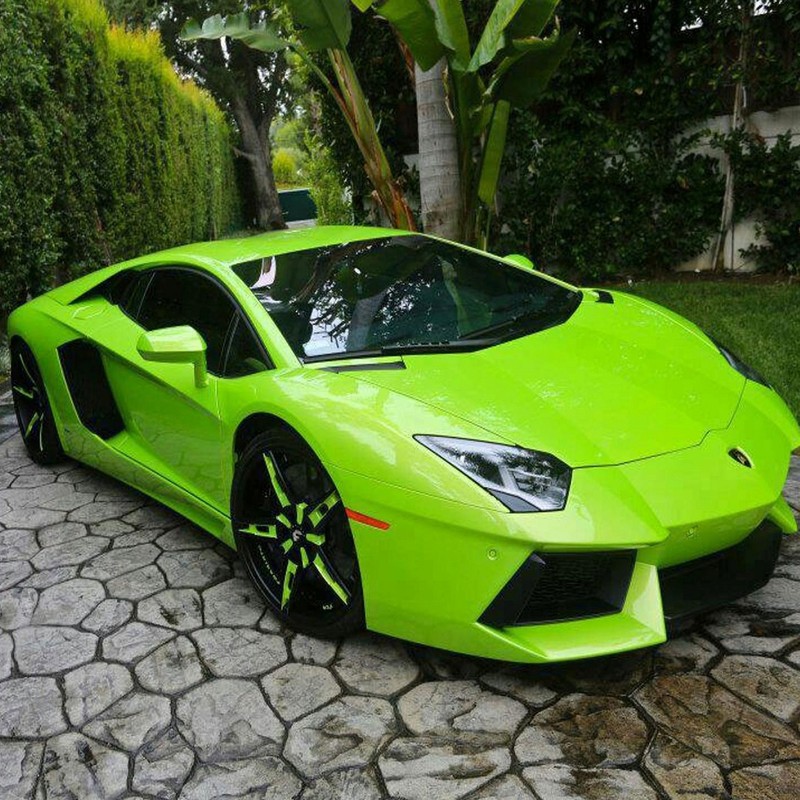 A lime green lambo parked in a driveway next to a tree (auto, car, super)