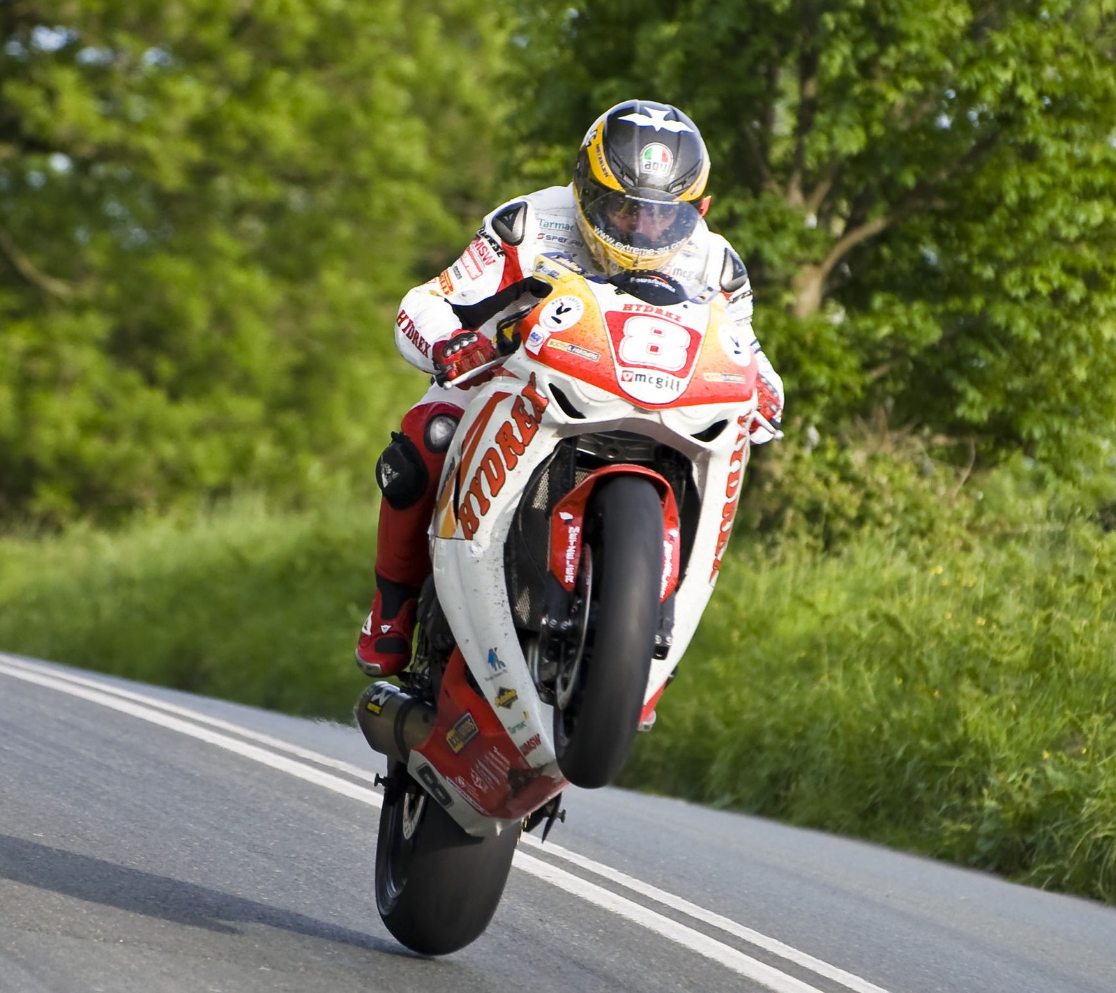 There is a man riding a motorcycle on a road with trees in the background (bike, motorcycle, race, superbike)