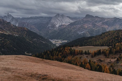 Uma vista de tirar o fôlego de uma paisagem montanhosa com uma cadeia de montanhas dramática, vales exuberantes e folhagem de outono sob um céu sombrio.