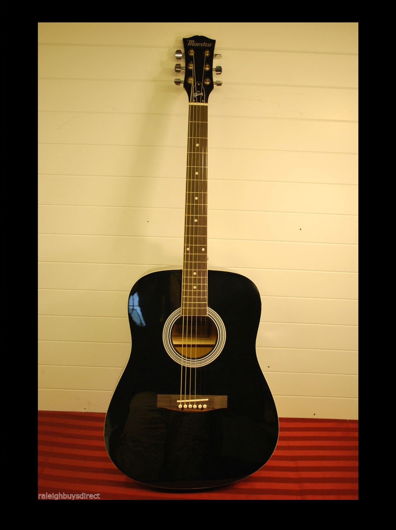 There is a black guitar sitting on a red table (guitar, music)