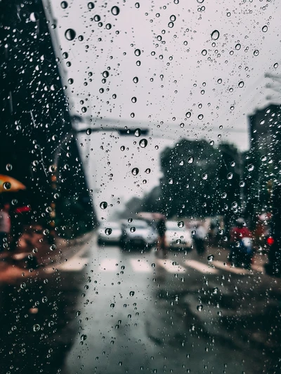 Regentropfen auf einer Windschutzscheibe, die die Sicht auf eine belebte Straße an einem stürmischen Nachmittag verschwommen machen.