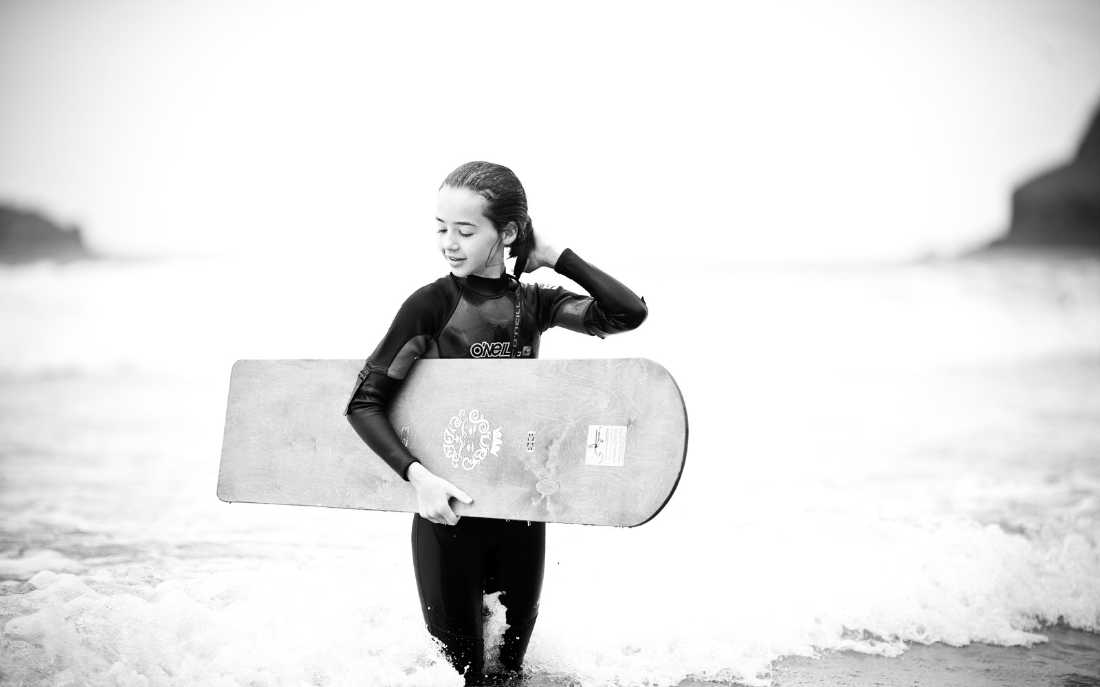 Surfista en traje de neopreno sosteniendo una tabla en las olas del océano en un día soleado (tabla de surf, diversión, blanco y negro, agua, onda de viento)