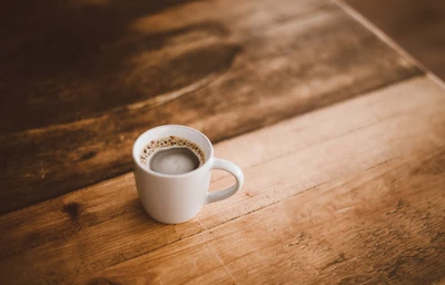 Una taza de café blanca se encuentra sobre una mesa de madera rústica, capturando la calidez de un momento de café por la mañana.