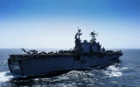 Amphibious assault ship navigating open waters with a helicopter on deck.