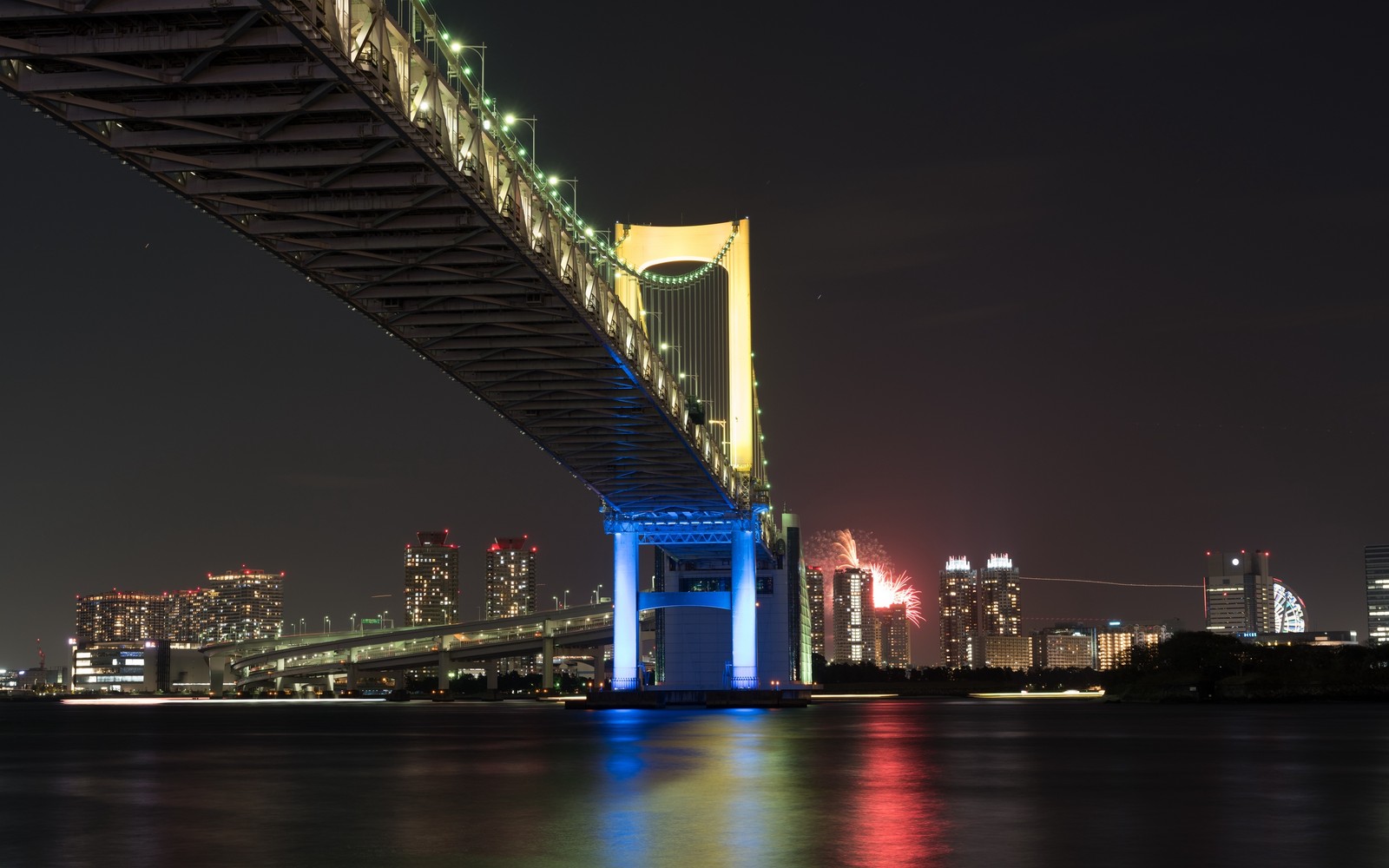 Uma vista curva de uma ponte com uma cidade ao fundo (noite, ponte, área urbana, cidade, marco)