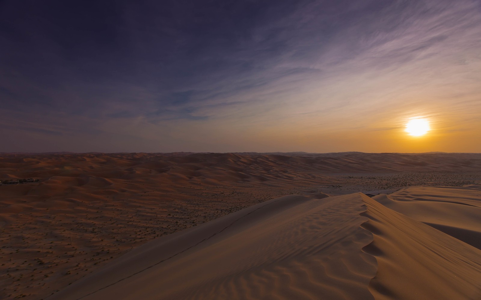 A view of a desert with a sun setting in the distance (erg, singing sand, dune, desert, sand)