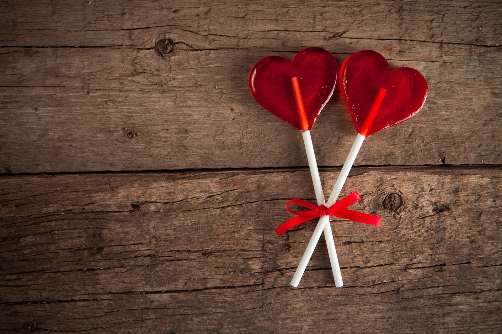 Deux sucettes rouges en forme de cœur attachées à une table en bois (cœur, rouge, amour, fleur, pétale)