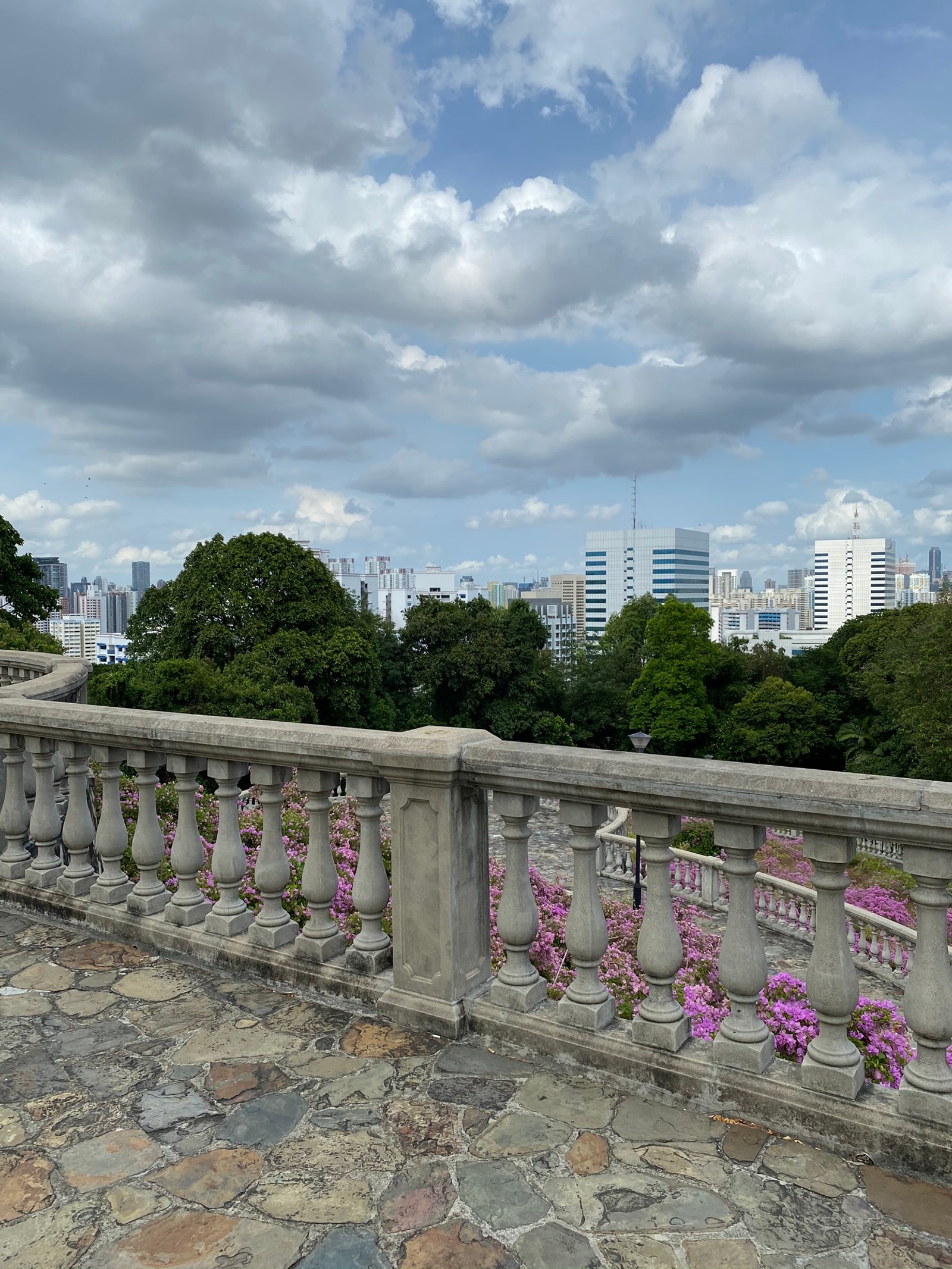 There is a stone balcony with a stone railing and flowers (fence, daytime, cloud, tower block, cumulus)