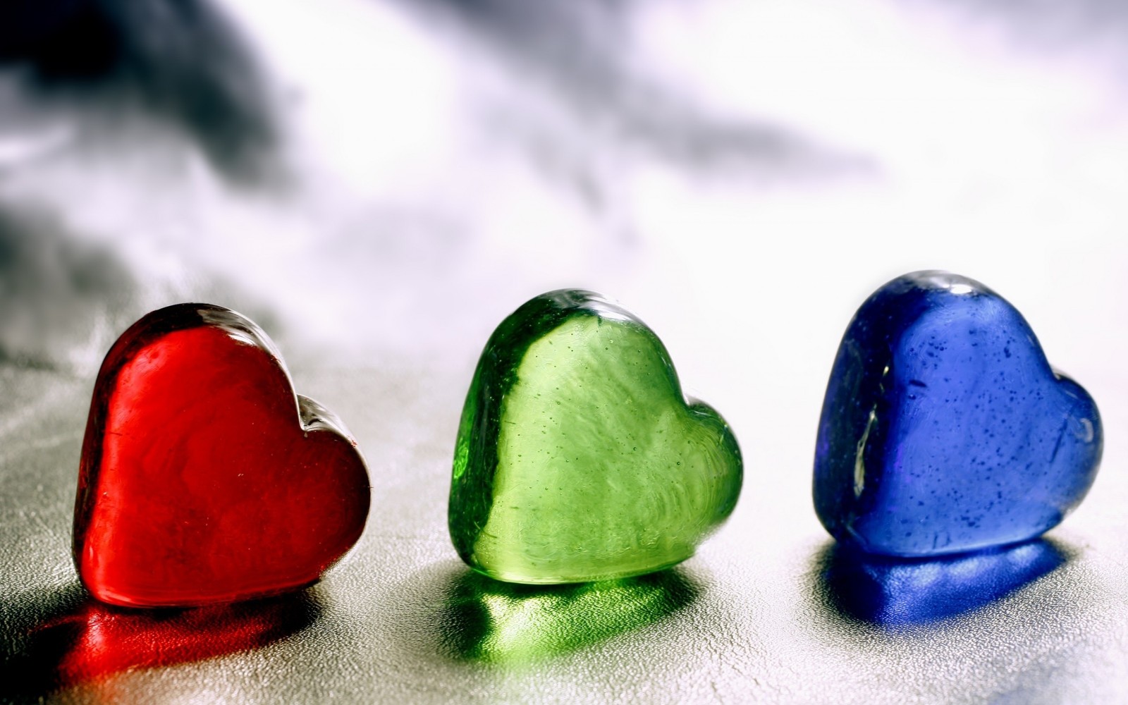 Three glass hearts are sitting on a shiny surface (heart, valentines day, macro photography, love, green)