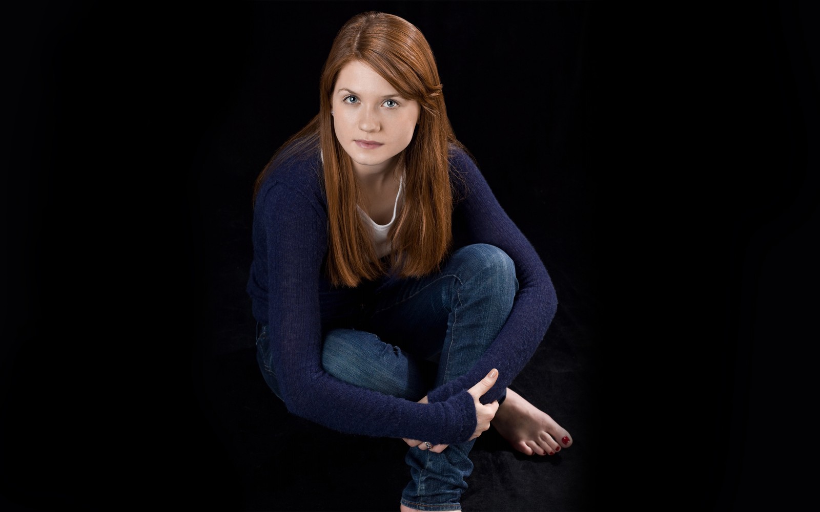 Une belle femme accroupie sur un fond noir (ginny weasley, harry potter, bleu, assis, beauté)