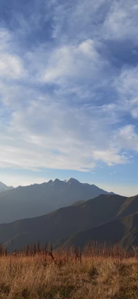 Cumbres montañosas majestuosas bajo un vasto cielo azul con nubes cúmulos y un primer plano de pradera