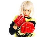 Rita Ora posiert selbstbewusst und zeigt übergroße rote Boxhandschuhe, gestylt in einem lebhaften Outfit mit einem kräftigen Lippenstift, das eine Fusion aus Mode und Athletik verkörpert.