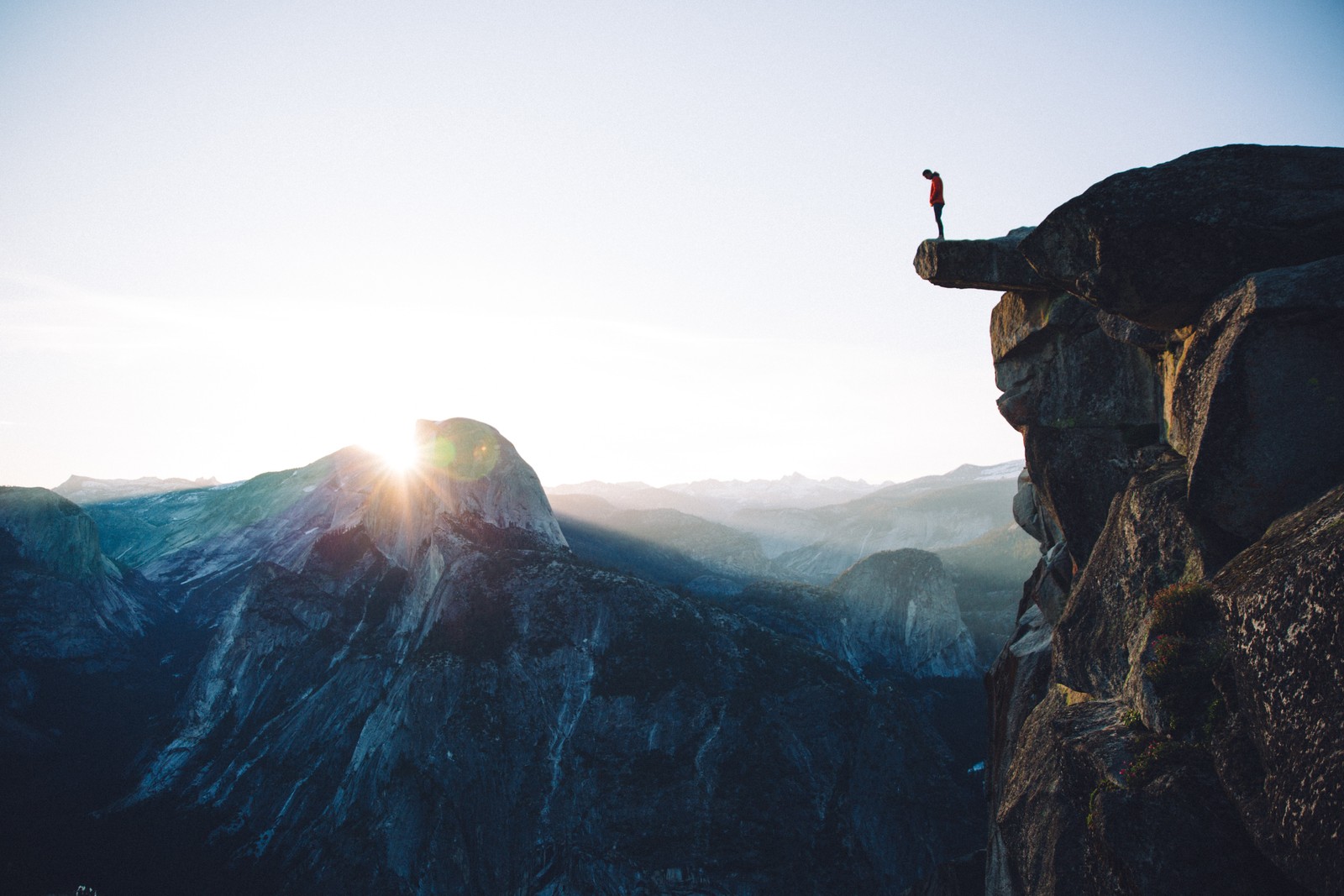 Eine giraffe steht auf einer klippe mit blick auf eine bergkette (sonnenlicht, base jumping, himmel, fallschirm, gebirgskette)