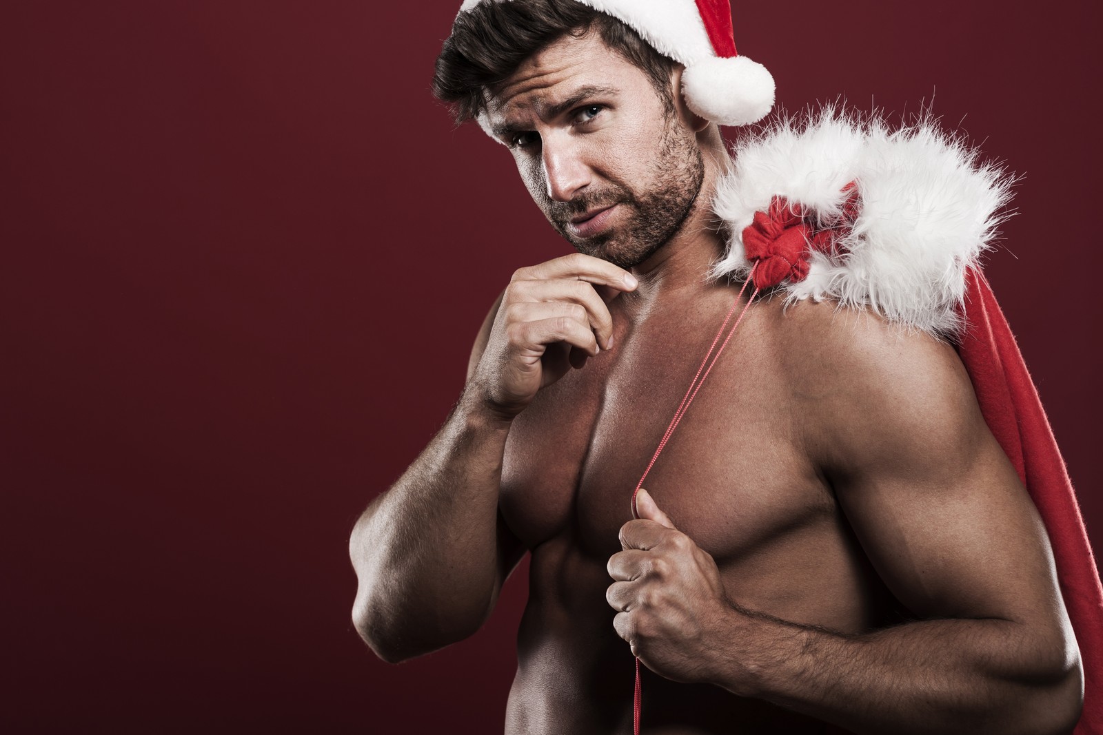 Un hombre con un gorro de santa posando para una foto (músculo, humano, pelaje, vello facial, aptitud física)