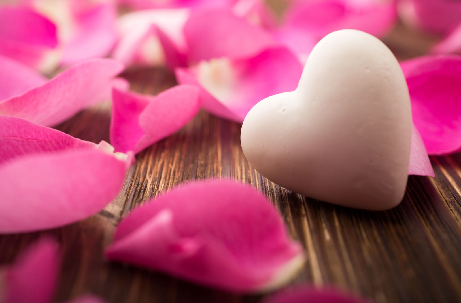 Il y a un objet en forme de cœur sur une table en bois entouré de pétales (cœur damour, cœur, romance, pétale, rose)