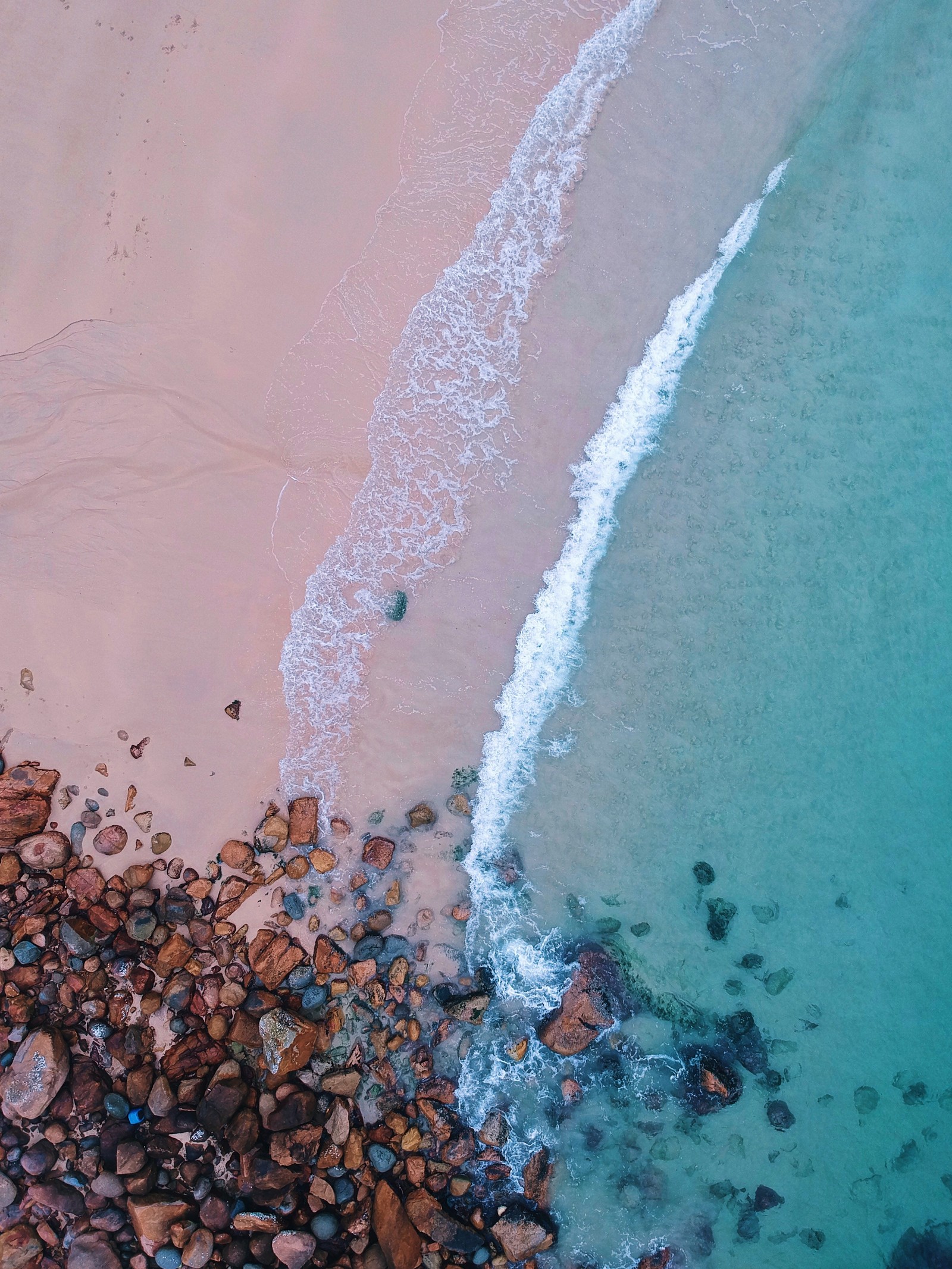 Vista aérea de uma praia com uma prancha de surf e pedras (água, mar, praia, linha, estuque)