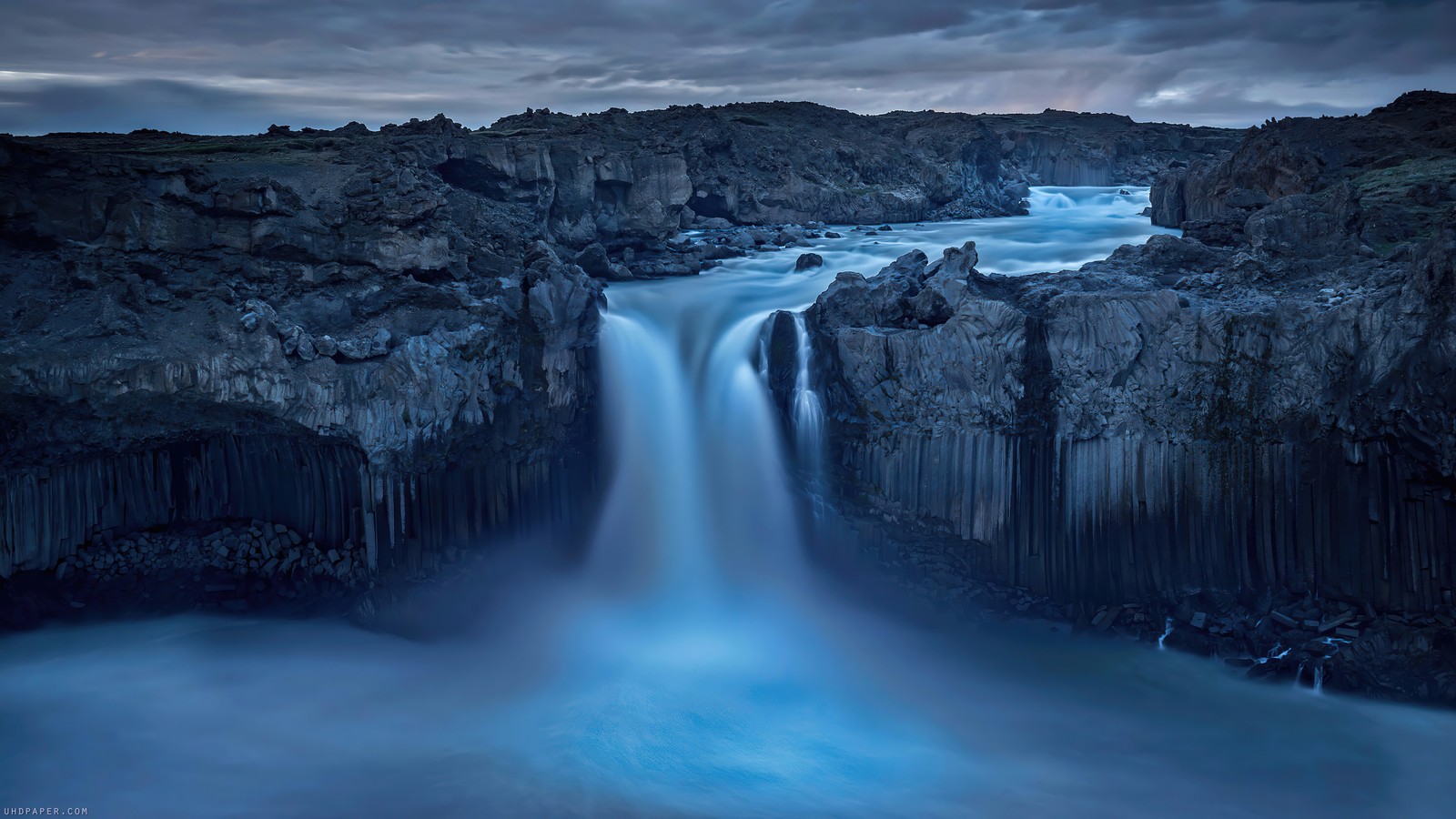 Una cascada que fluye hacia un cuerpo de agua rodeado de rocas (cascada, rocky, lansdscape, escenario)