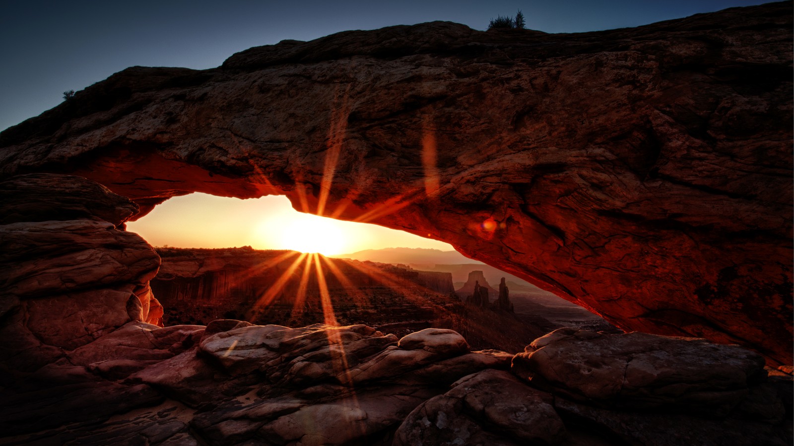 A close up of a rock formation with the sun setting behind it (mesa arch, park, national park, canyon, rock)