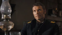 Sam Worthington retrata a un oficial militar contemplativo en un entorno tenuemente iluminado, mostrando un momento crucial en "Horizonte: Una saga americana".