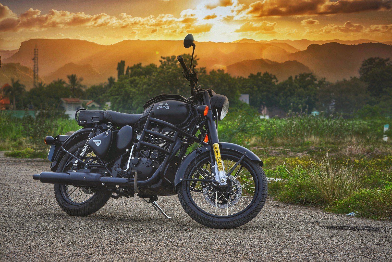 Una motocicleta aparcada en un camino de tierra con una puesta de sol de fondo (500, negro, clásico, enfield, año nuevo 19)