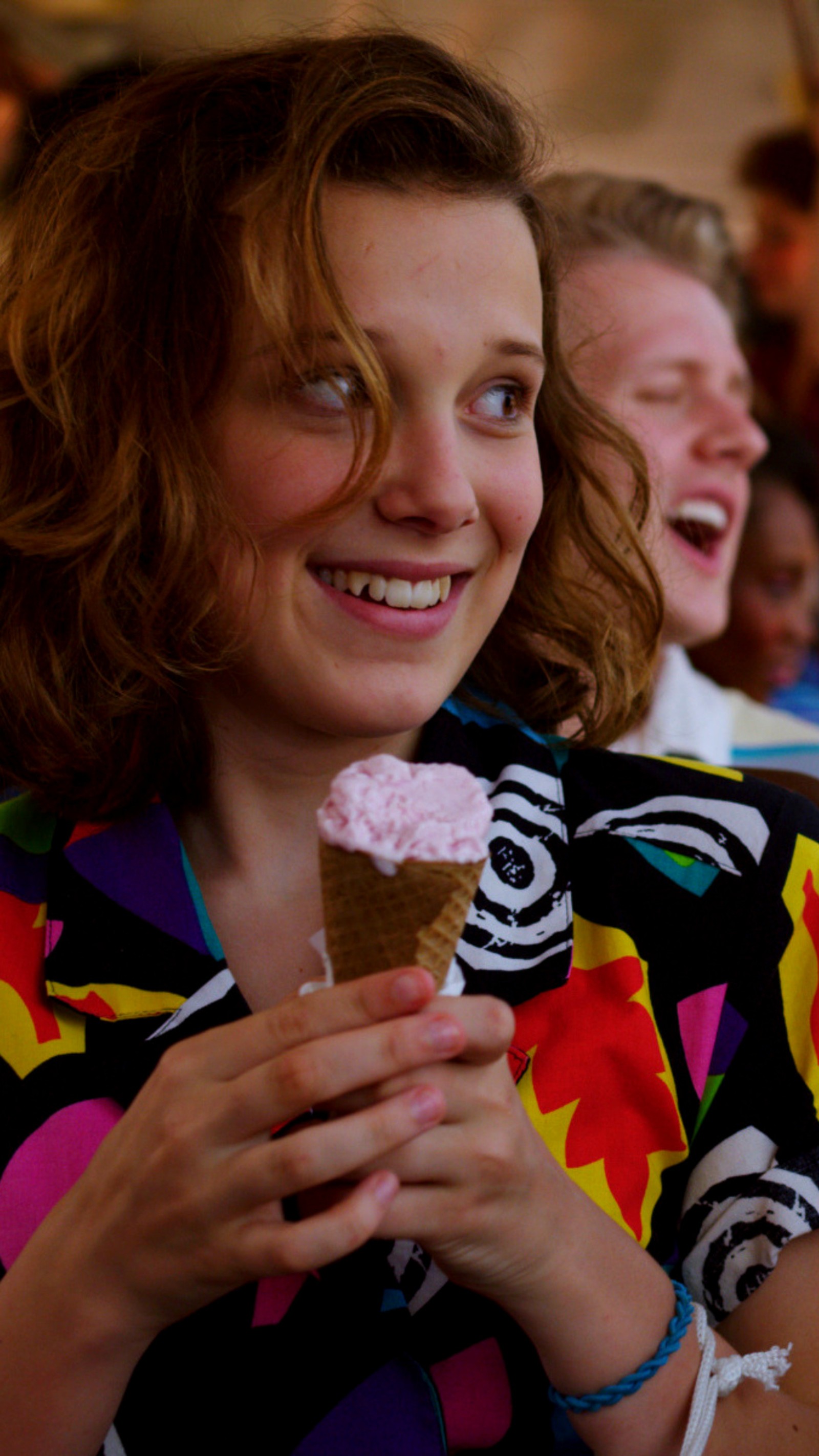 Una mujer sonriente sosteniendo un cucurucho de helado con glaseado rosa (once, millie, stranger things)