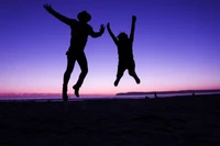 Silhouettierte Paare, die bei Sonnenuntergang am Strand springen