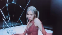 Rosé from BLACKPINK poses confidently in a striking outfit, surrounded by shattered glass, exuding an edgy and powerful vibe.