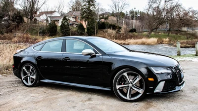 Sleek black Audi RS 7 Sportback parked by the water, showcasing its stylish design and powerful stance.