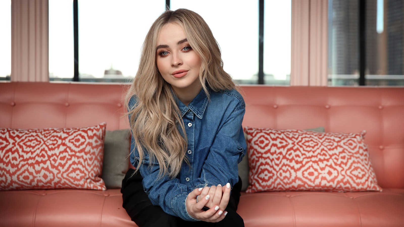 Un primer plano de una mujer sentada en un sofá con una almohada roja (sabrina carpenter, estadounidense, cantante, celebridad, chicas)