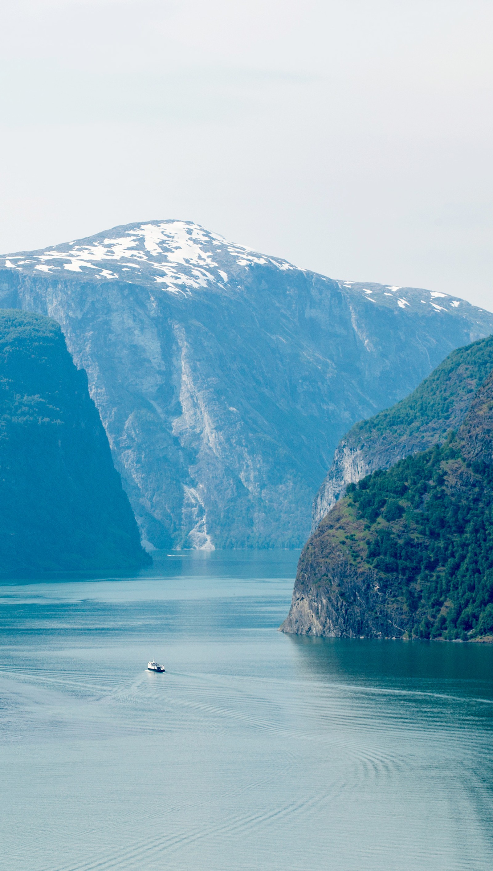 Há um barco flutuando na água perto de uma montanha (fiorde, paisagem, montanhas, natureza, noruega)