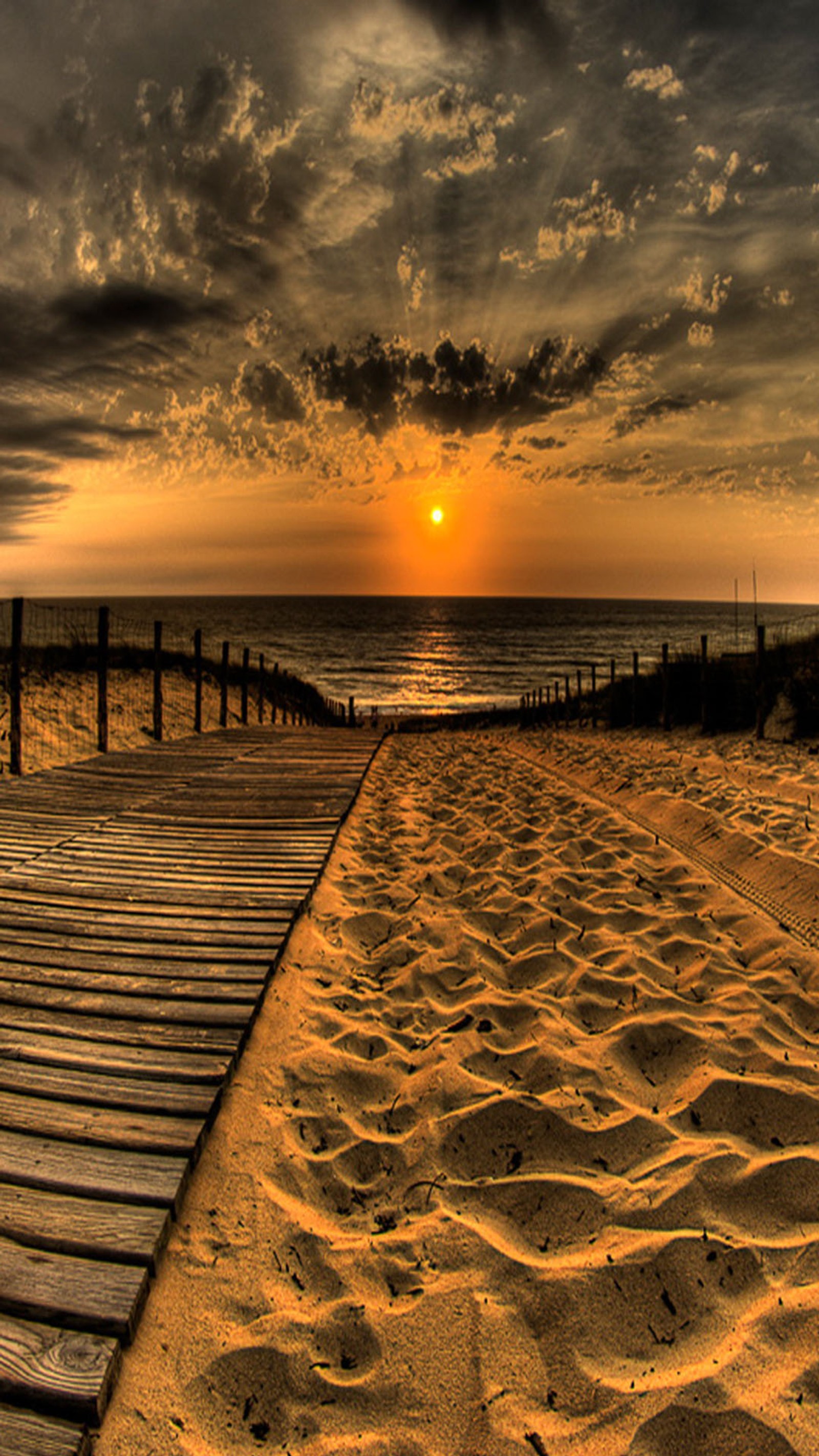 Un paseo marítimo que lleva a la playa al atardecer con nubes (arena, mar)