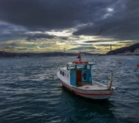 Ein ruhiges Boot, das im Bosporus vor Anker liegt, mit einem dramatischen Himmel und der Silhouette einer Brücke im Hintergrund.