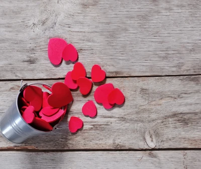 Corazones rojos esparcidos de un cubo plateado sobre una superficie de madera