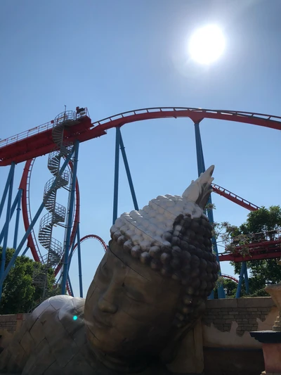 Estatua de Buda pasada por alto por una emocionante montaña rusa bajo un brillante sol