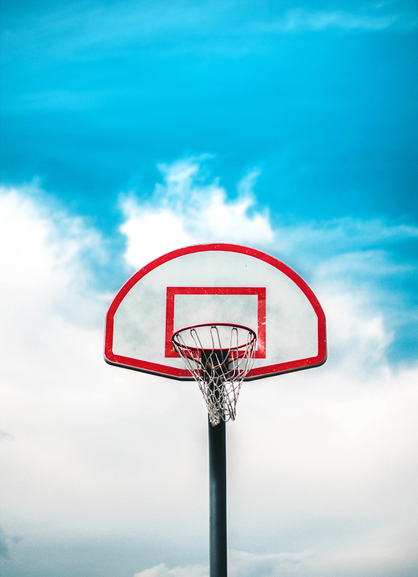 There is a basketball hoop with a red rim and a blue sky (basketball, backboard, basketball hoop, basketball court, cloud)