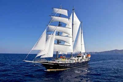 Majestuoso barco de vela navegando graciosamente por el océano azul, mostrando sus impresionantes velas contra un cielo despejado.