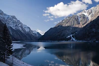 Lago glacial sereno refletindo majestosas cadeias de montanhas sob um céu claro.