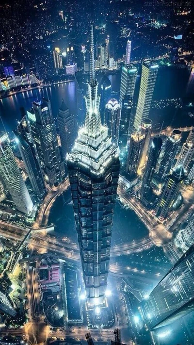 Aerial view of a vibrant city skyline at night, featuring a striking illuminated skyscraper surrounded by modern buildings and busy streets.