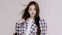 Lee Na Gyung do Fromis 9 exibindo seu visual estiloso e cabelo longo em um traje chique contra um fundo suave e listrado.