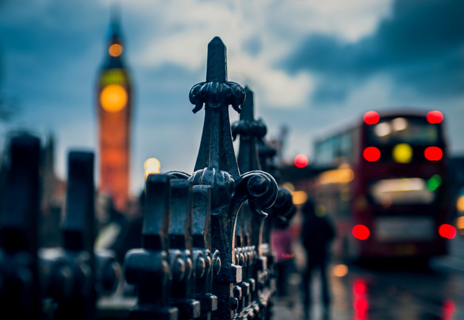 There is a bus that is driving down the street in the rain (big ben, city, night, evening, reflection)