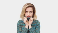 Kiernan Shipka in a patterned sweater, playfully pulling up the collar.