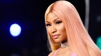 Nicki Minaj mit langen pinken Haaren und glamourösem Make-up in einer lebhaften Umgebung.