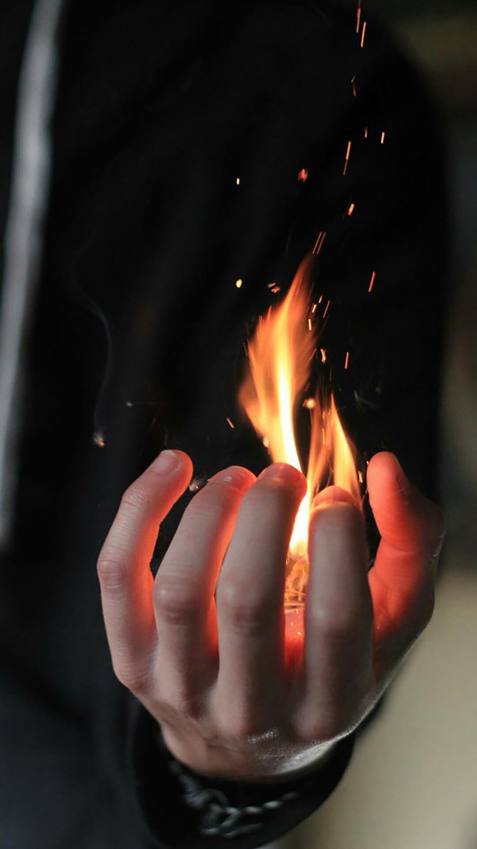 Someone holding a lit match in their hand with a black background (fire, fra)