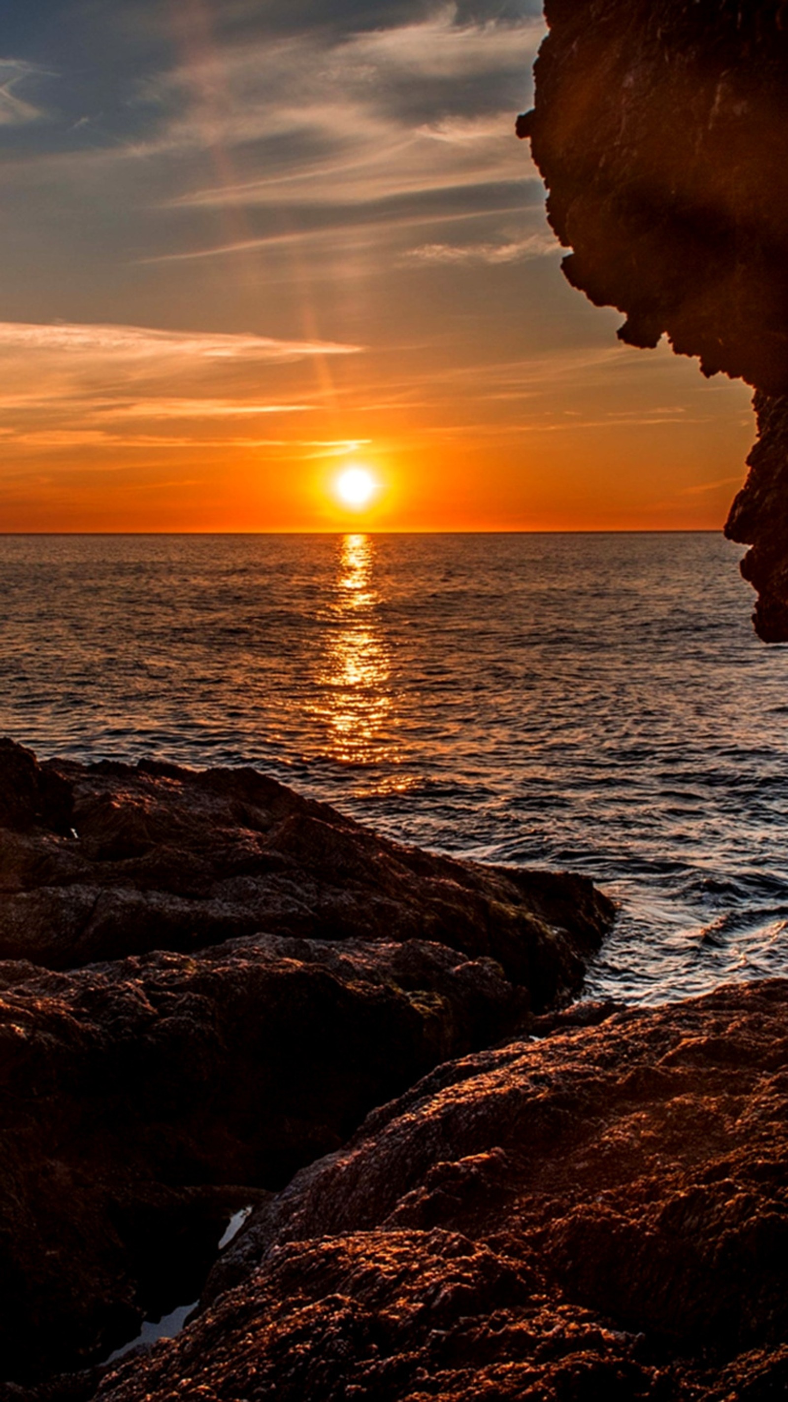 Sunset over the ocean with a person standing on a rock (beach, breathtaking, majestic, sea, sunset)