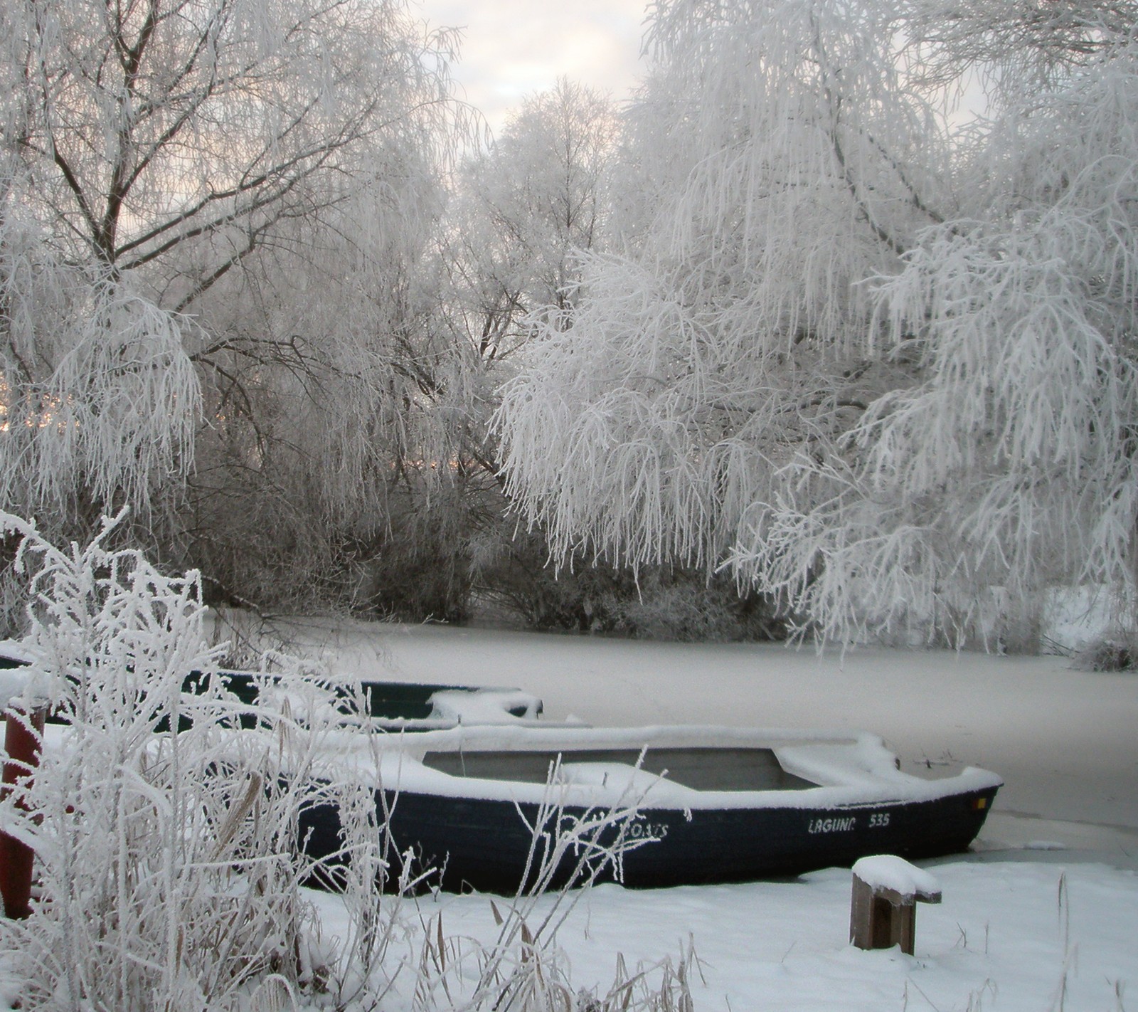 There is a boat that is sitting in the snow by the water (snow, winter)