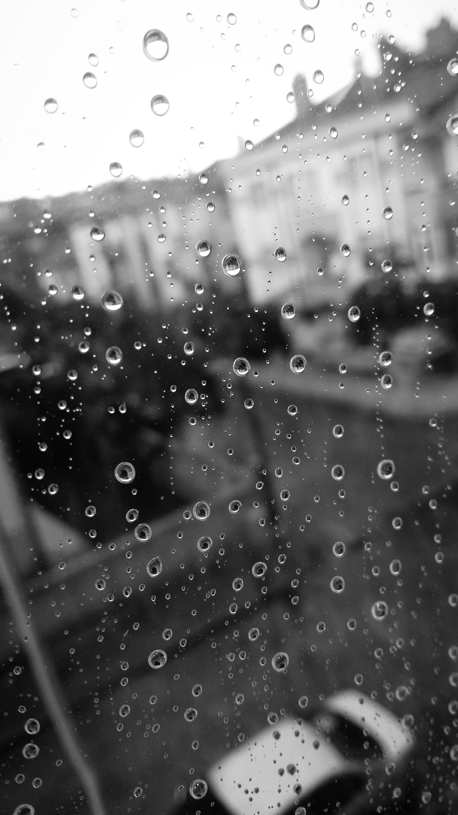 Primer plano de un coche estacionado frente a una ventana con gotas de lluvia (gota, gotas, borde, silueta)